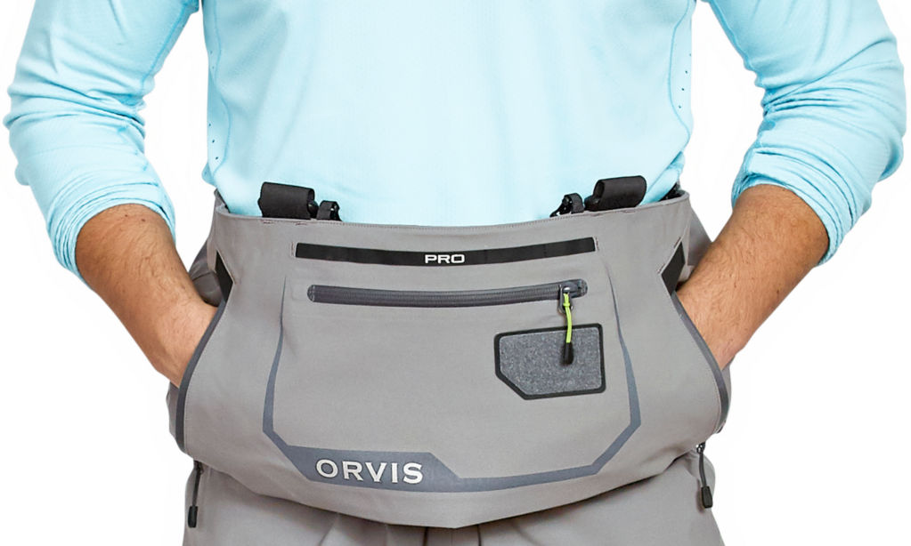 An angler wearing Orvis PRO Waders places their hands in the kangaroo pocket.