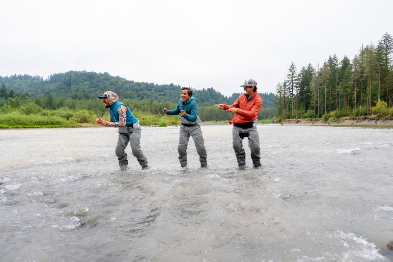 Three people in waders laughing in a stream.