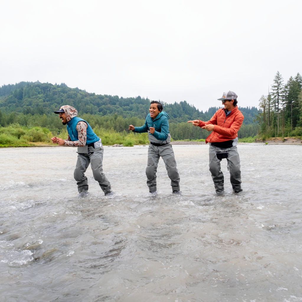 Three people in waders laughing in a stream.