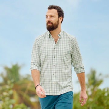 Man in tech chambray shirt walks down a beach.