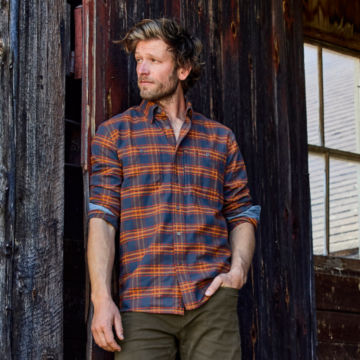 Man in a Navy Flat Creek Tech Flannel leans up against a barn door.