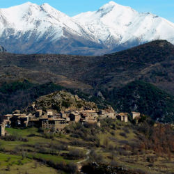 A village of brown stone buildings nestles under the shadow of snow-capped mountains