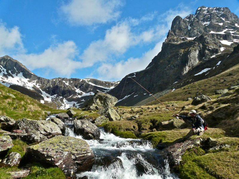 An angler fishes a rocky stream in the snow-tipped mountains of Spain.