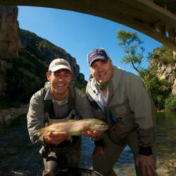 Two men holding a fish beneath an arched stone bridge