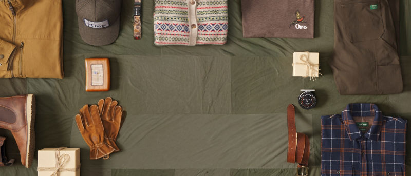 A collection of gifts with such as a ball cap, sweater, and leash laid neatly on an olive green cloth background.