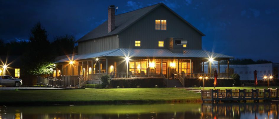 A scenic lodge lit up with warm lights set on a lake at night.