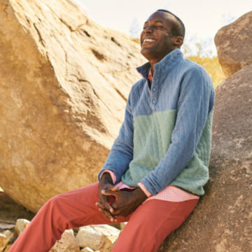 A man wearing a Quilted Colorblock Sweatshirt laughs against a rock.