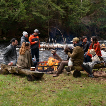 A group of friends gathers around an Orvis Fire Ring with their dogs.