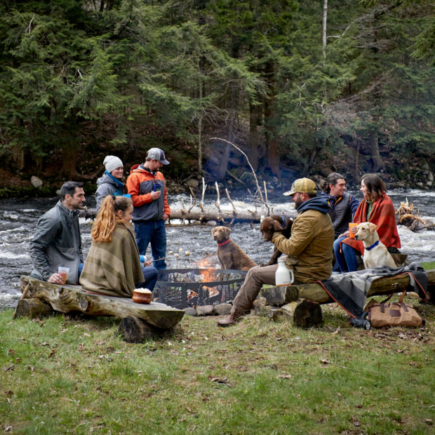 A group of people sitting around a campfire by the bank of a river