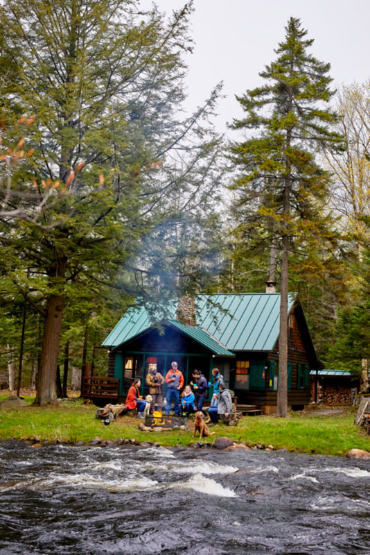 A group of people sitting around a campfire by the bank of a river.