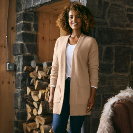 A woman stands in front of a fireplace wearing a cardigan