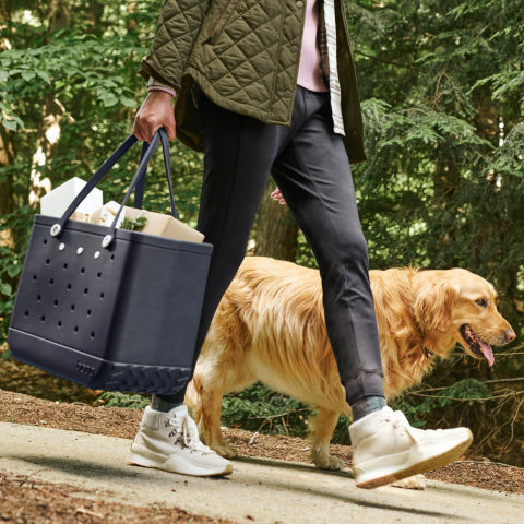 A woman carries a blue tote full of wrapped gifts down. a path with her golden retriever