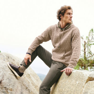 Man in Natural Heather Outdoor Quilted Hooded Sweatshirt sits on a rock.