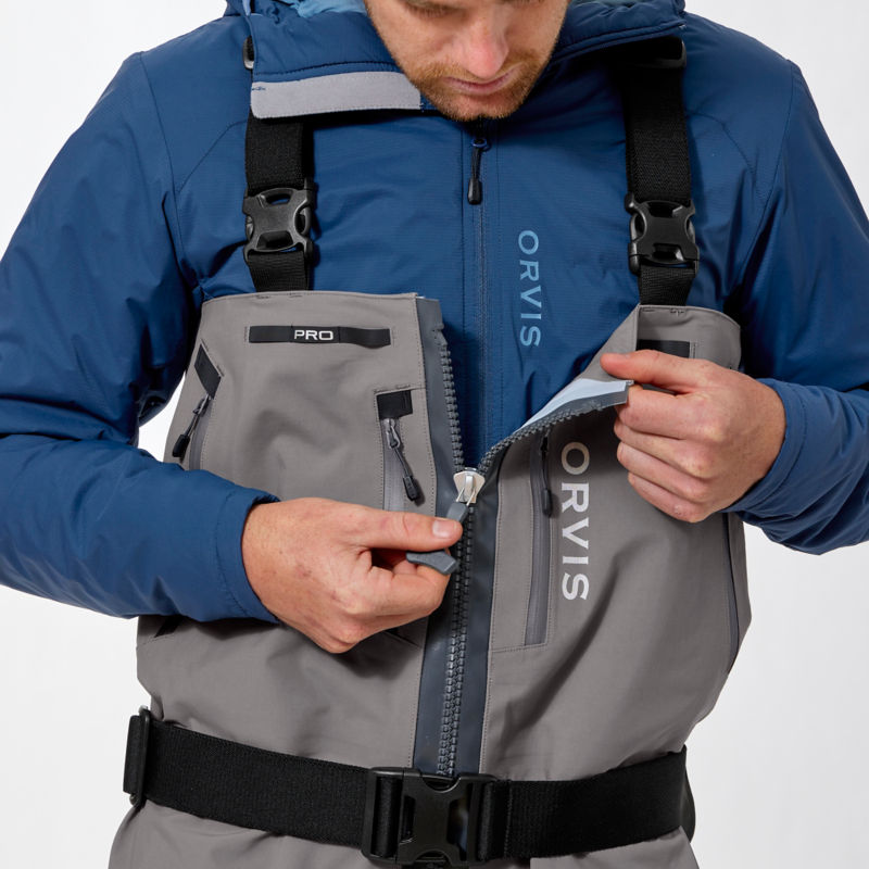 An angler wearing Orvis PRO Waders unzips the main zipper.