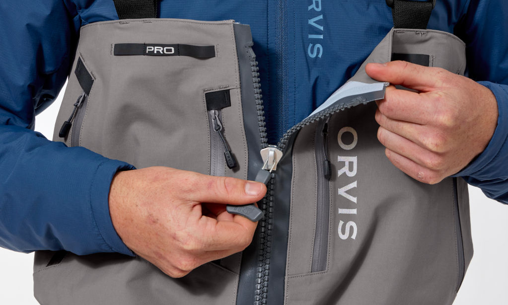 An angler wearing Orvis PRO Waders unzips the main zipper.