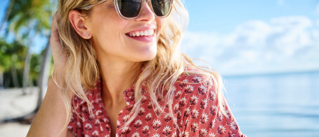 A close up of a blonde woman wearing sunglasses and a bright red printed shirt.