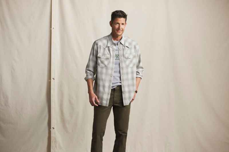 A model wearing a plaid button-up shirt jacket over a T-shirt and dark green pants.