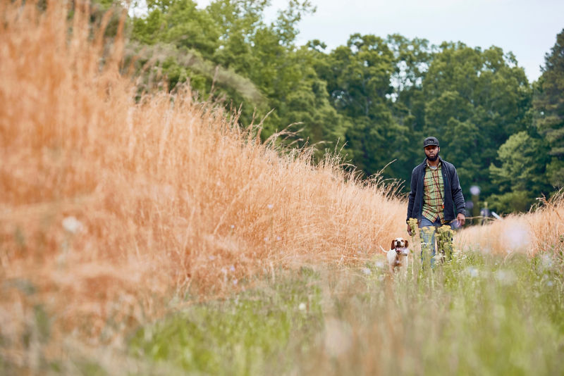 Durrell Smith Walks through a field of dry grass with his dog.