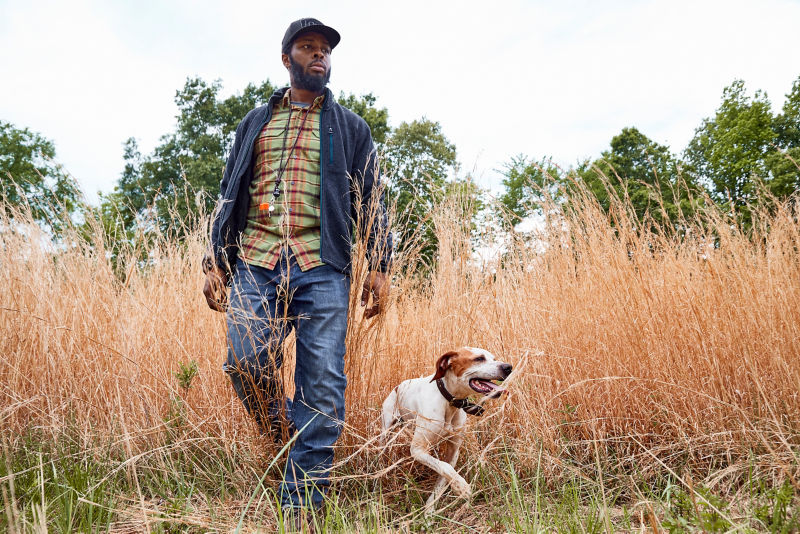 A man and a dog walking through a field of dry grass.