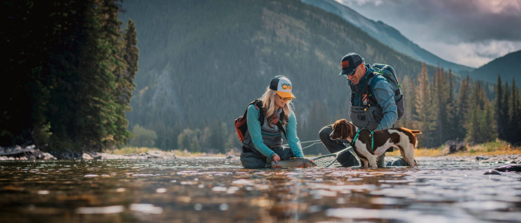 Timbre and D'Arcy with their dog, North, release a fresh-caught fish back into a river