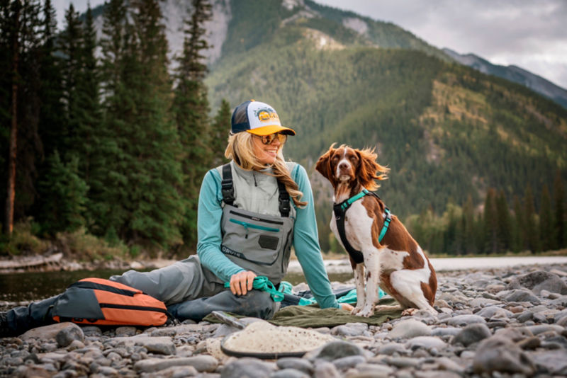 A woman and her dog sitting on river rocks in the mountains