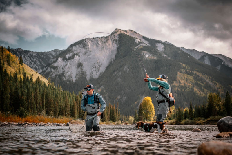 D'Arcy and Timbre wade in a river with their dog while fishing