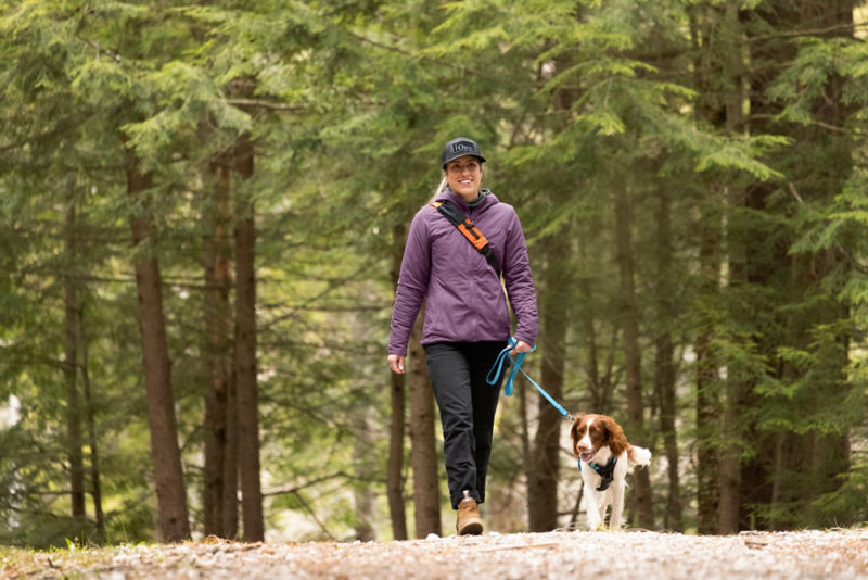 A woman walking her dog on a leash in the woods