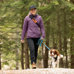 A woman walking her dog on a leash in the woods