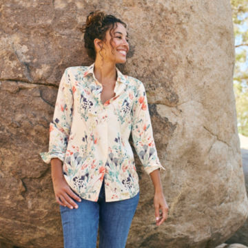 Woman in White Everyday Printed Silk Shirt leans against a rock.