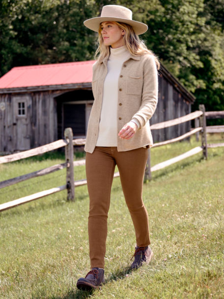Woman in Boiled Cashmere Sweater Jacket walks along a wooden fencepost in a field.