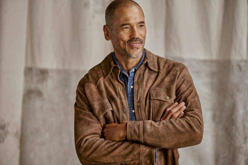 A model wearing a dark suede jacket with his arms crossed.