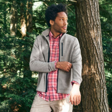 Man in Grey Lewiston Merino Full-Zip Sweater walks through the woods.
