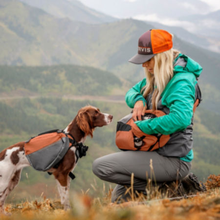 While on a hike, a woman is bending down giving her dog a treat