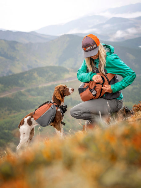 Woman and dog loaded with Tough Trail™ gear stop to have a snack on a steep, rocky trail.