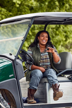 Ashley Smith, sitting in a golf cart wearing a flannel shirt and jeans, kicking her feet up and laughing