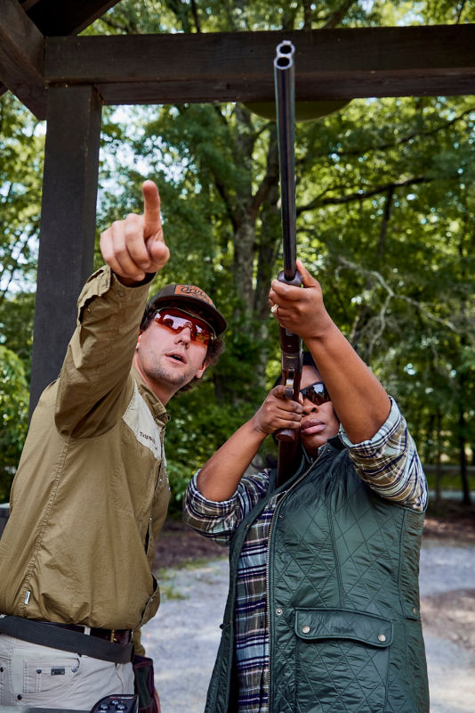 A shooting instructor points as a student aims