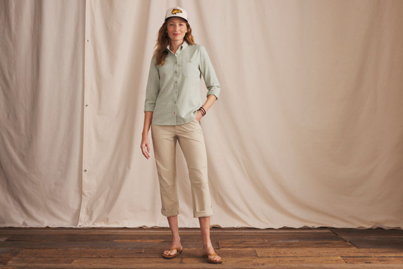 A woman wearing a light green button-down shirt over cream colored pants and a flipflops.