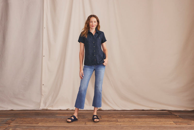 A smiling woman wearing a patterned blue short sleeve button-down shirt.