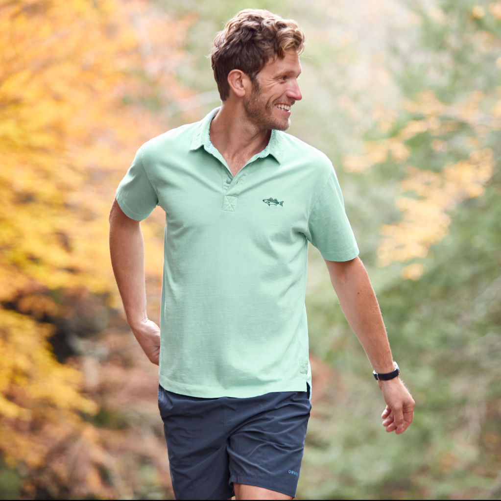 Man smiles as he walks through the woods in polo and shorts.