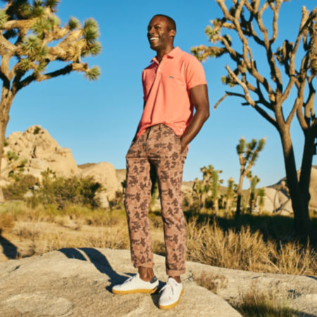 A man wearing an orange performance polo and 1971 camo chino pants on a rock in the desert.
