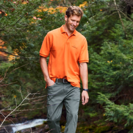 A man in front of pines wearing an orange signature polo