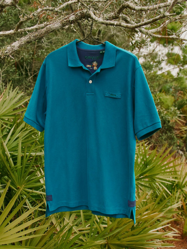 A gorgeous teal polo hanging on a tree in the woods.