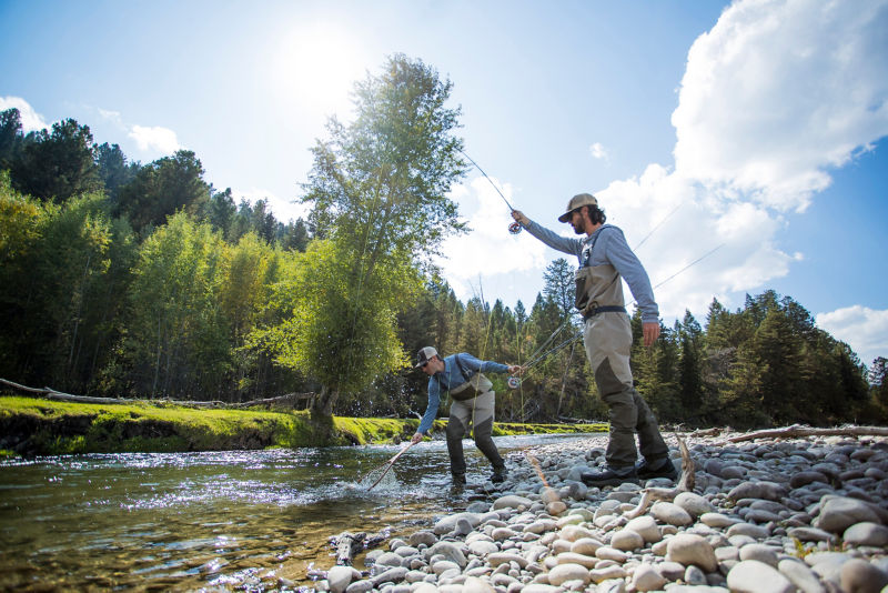 Jackson Hole Fly Fishing School netting a fish in a rocky river.