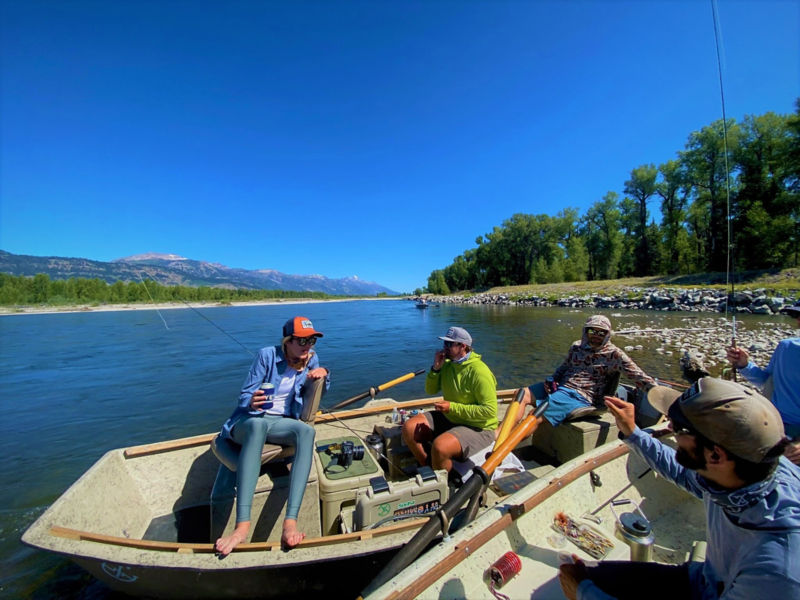 Two drift boats filled with people on a river in Wyoming under a brilliant blue sky.