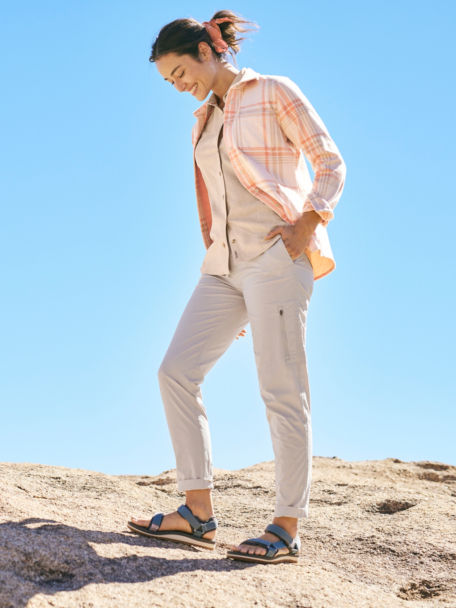 Woman in Sandcastle Short-Sleeved Tech Chambray Shirt walks along a rock in her sandals in the desert.