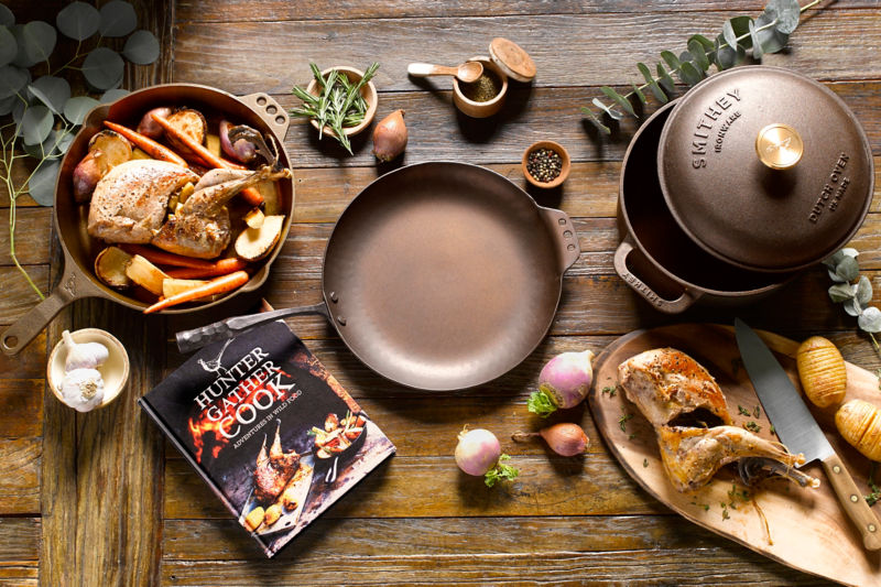 A collection of chefs tools from garlic and pots to cookbook and onions.