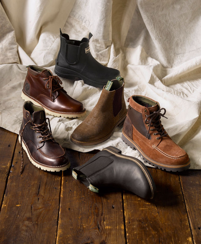 A collection of Barbour shoes and boots laid out on a wooden floor and canvas.