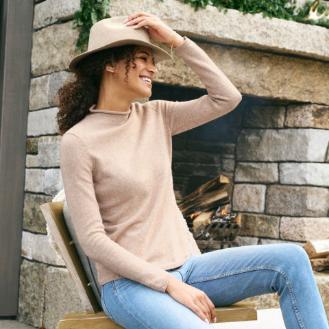A model in a tan cashmere sweater and jeans adjusts her fedora