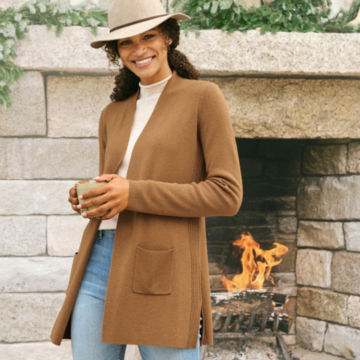 Woman in Anywhere Cardigan holds a cup of coffee beside a fireplace.