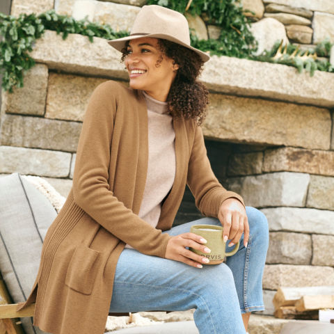A model in a tan fedora sits on a lounge chair's arm